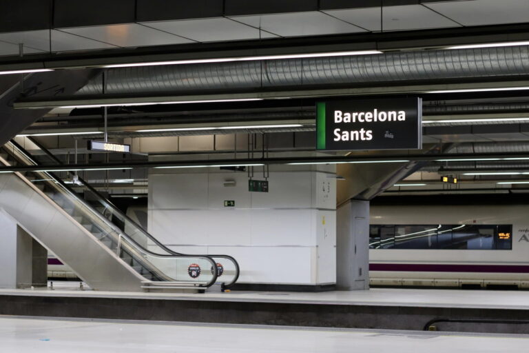 Roltrap op station Barcelona Sants met lege perrons en een trein op een van de perrons.