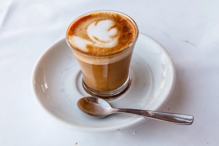 Koffie met melk in een glas met een lepeltje op een wit schoteltje. Spaanse cortado - espresso koffie met melk