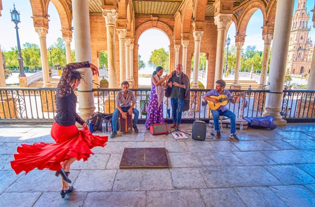 Een flamencodanseres in een rode rok en zwarte top voert een energieke dans uit voor muzikanten onder een overdekte arcade. Flamenco straatoptreden in Sevilla.