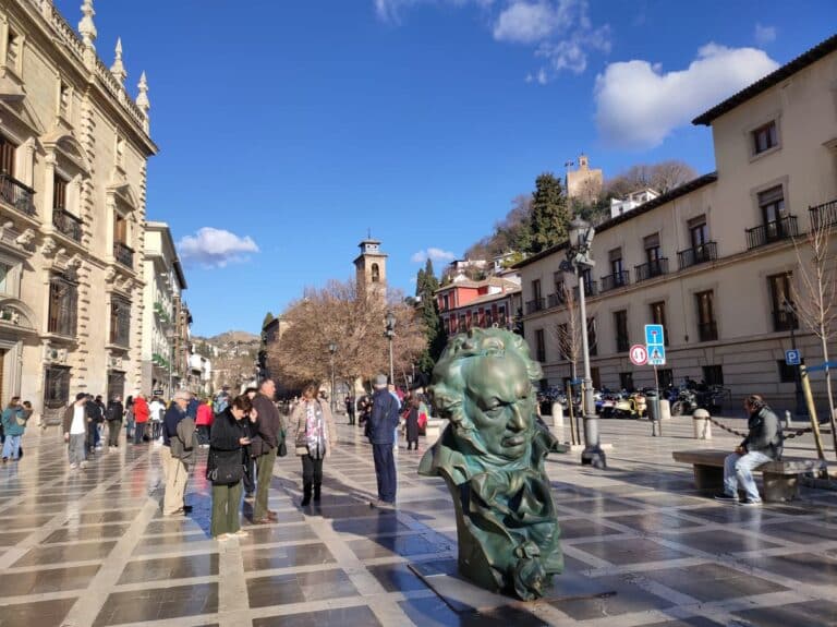 Grote groene buste van Francisco de Goya op een plein in Granada, met mensen en gebouwen op de achtergrond.
