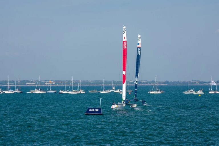 Twee SailGP F50-catamarans varen op zee tijdens een race, met toeschouwersboten op de achtergrond.