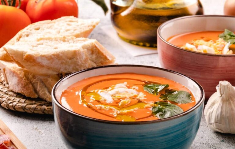 Twee kommen met salmorejo, een traditionele koude soep uit Andalusië, gemaakt van tomaten, brood, olijfolie, azijn en knoflook, met een dikke en romige structuur, geserveerd koud en gegarneerd met gekookt ei en jamón (Spaanse gedroogde ham).