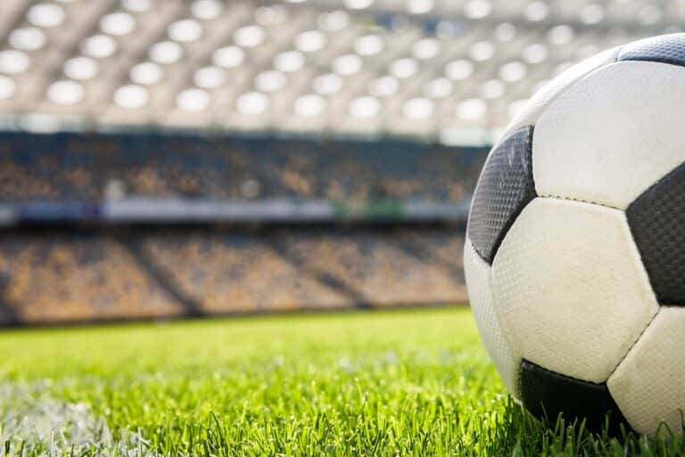 Voetbal op het gras in een leeg stadion, met tribunes op de achtergrond.