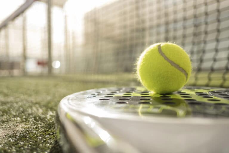 Close-up van een padelbal op een padelracket met het net en de padelbaan op de achtergrond