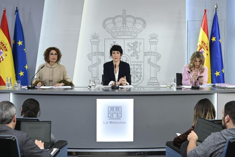 Drie ministers tijdens een persconferentie na de ministerraad in La Moncloa, met Spaanse en EU-vlaggen op de achtergrond en journalisten op de voorgrond.