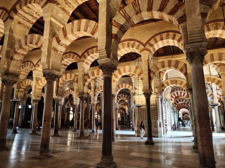 Interieur van de Mezquita-kathedraal in Cordoba met rood-witte hoefijzerbogen en rijen stenen zuilen.