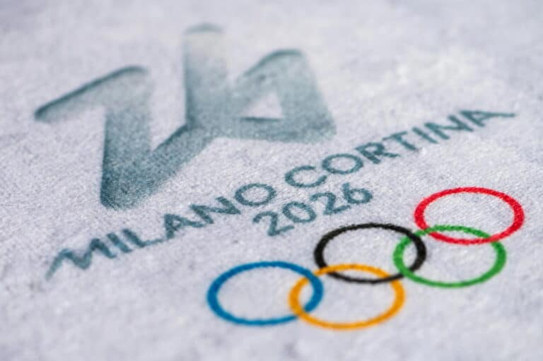 Detail van een stoffen oppervlak met de tekst ‘Milano Cortina 2026’ en de olympische ringen.