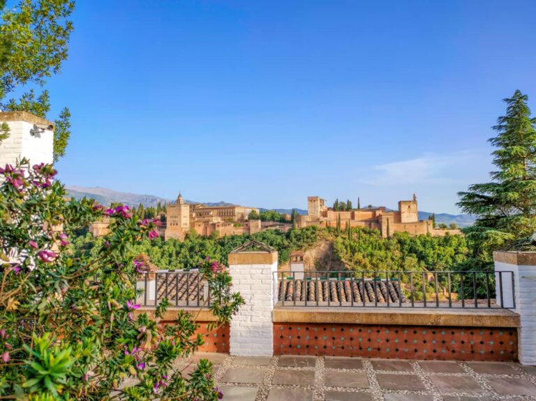 Uitzicht op het Alhambra in Granada, met paleizen en vestingmuren op een beboste heuvel.