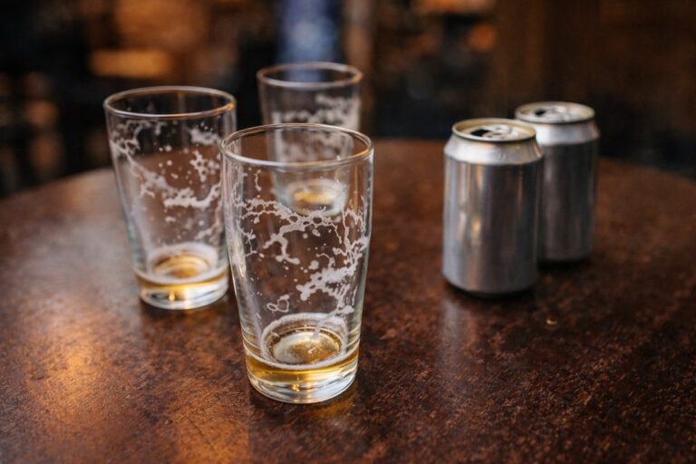 Lege bierglazen en aluminium blikjes op een houten tafel.