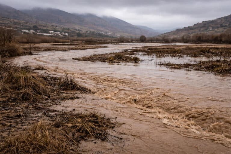 Modderige rivier die buiten haar oevers is getreden en landbouwgrond onder water zet in een landelijk gebied.