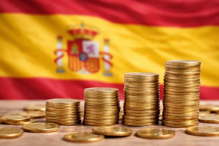 Stapels euromunten op een tafel met de Spaanse vlag onscherp op de achtergrond.