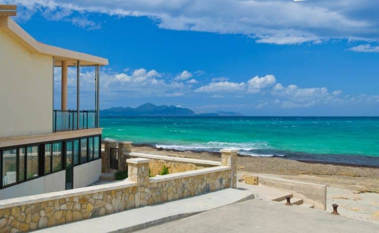 Vakantiewoning aan de kust op Mallorca met uitzicht op zee, een terras en een stenen afscheiding langs het strand.