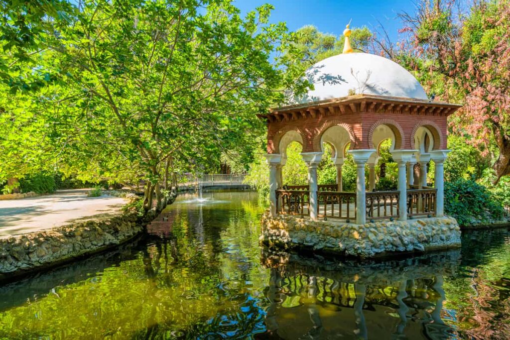 Paviljoen met koepel in het Parque de María Luisa in Sevilla, omgeven door water en bomen.
