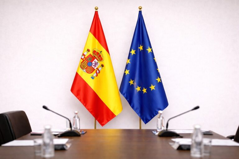 Spaanse vlag en EU-vlag in een neutrale vergaderruimte met tafel, microfoons en documenten op de voorgrond