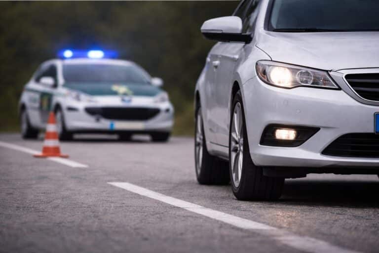 Witte personenauto op de voorgrond op een tweebaansweg met een Guardia Civil-politieauto met blauwe zwaailichten en een verkeerskegel op de achtergrond