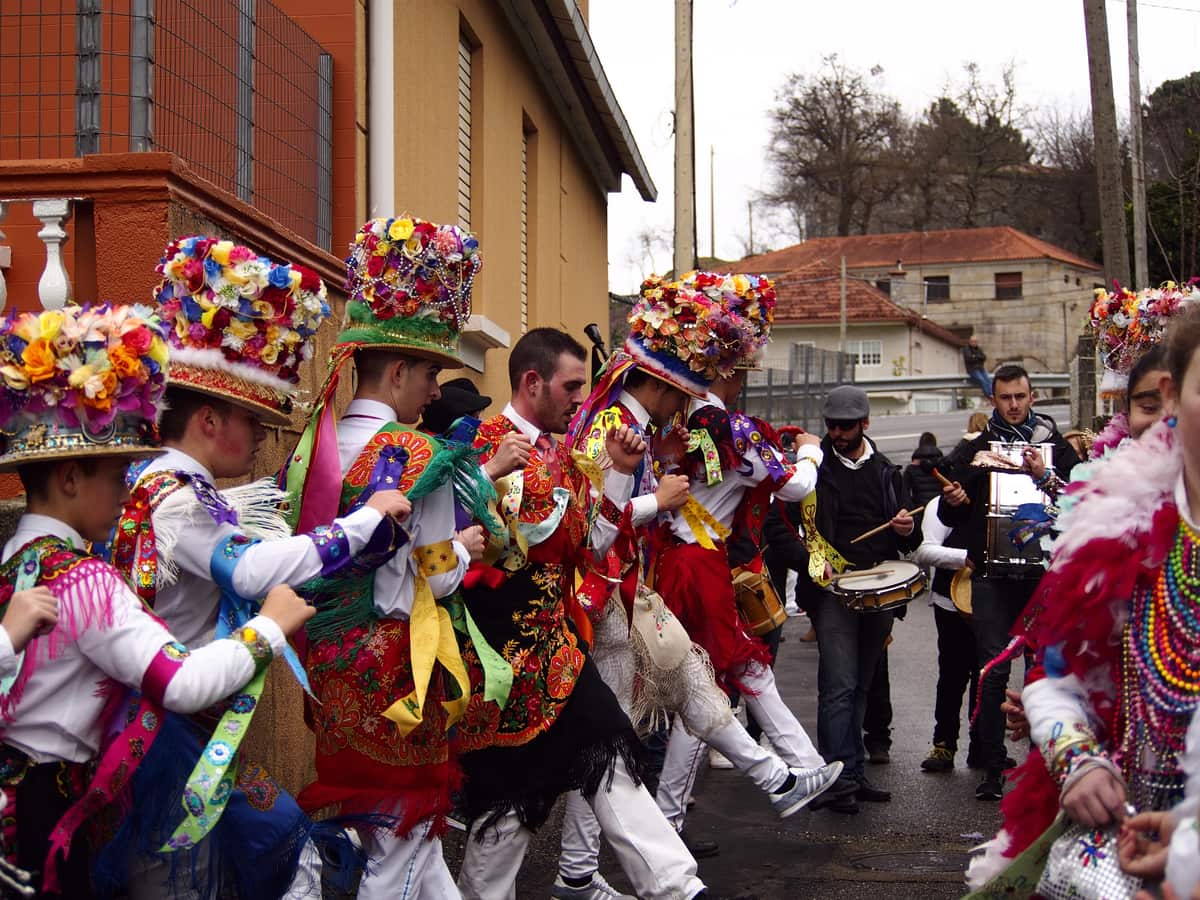 Deelnemers in kleurrijke traditionele kostuums dansen op straat tijdens het Entroido de Cobres, begeleid door muzikanten met trommels.