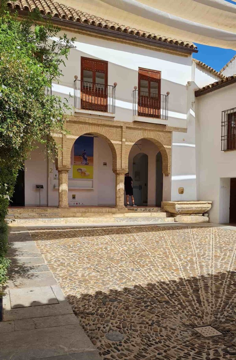 Binnenplaats van de Casa Mudéjar in Córdoba met geplaveide stenen vloer, hoefijzerbogen op zuilen en een witgekalkte gevel met houten balkons.