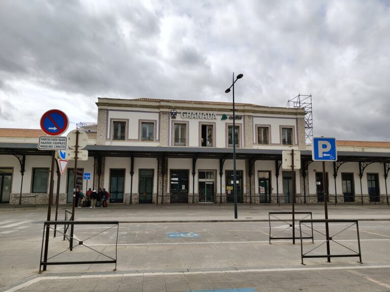 Voorgevel van station Granada onder een bewolkte hemel, met de stationsnaam boven de ingang en enkele reizigers bij de entree