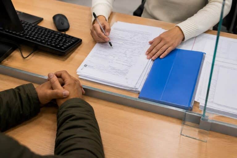Handen en documenten op een loket van een immigratiedienst tijdens een administratieve aanvraag.