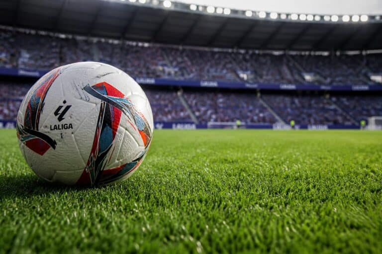 Close-up van een voetbal op groen stadiongras met tribunes op de achtergrond