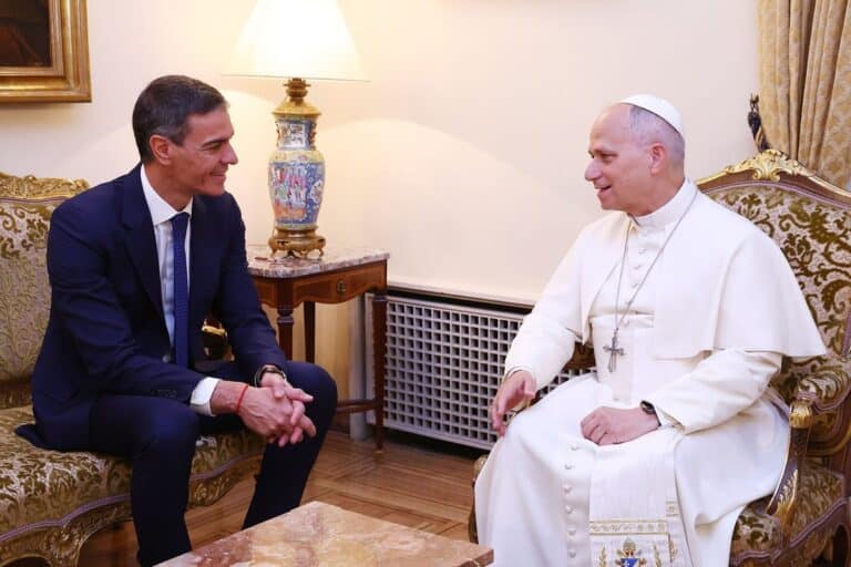 De Spaanse premier Pedro Sánchez zit tegenover paus Leo XIV tijdens een ontmoeting in een salon van de Apostolische Nuntiatuur in Madrid. Beide mannen voeren een gesprek terwijl zij tegenover elkaar in fauteuils zitten. Op de achtergrond staat een tafellamp op een houten bijzettafel.