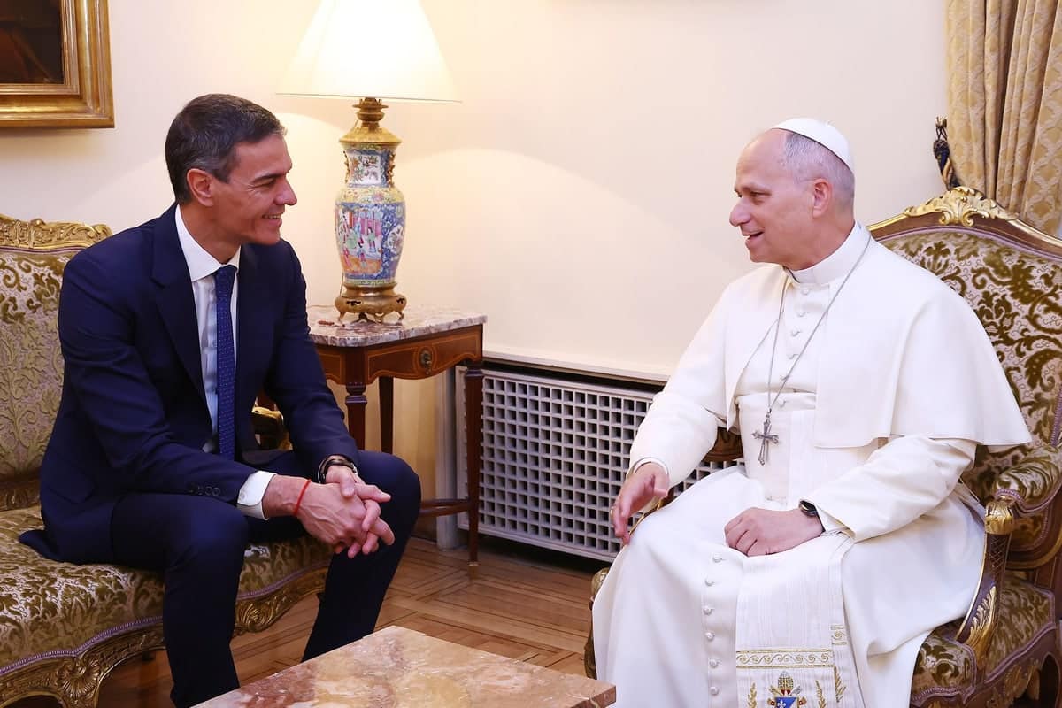 De Spaanse premier Pedro Sánchez zit tegenover paus Leo XIV tijdens een ontmoeting in een salon van de Apostolische Nuntiatuur in Madrid. Beide mannen voeren een gesprek terwijl zij tegenover elkaar in fauteuils zitten. Op de achtergrond staat een tafellamp op een houten bijzettafel.