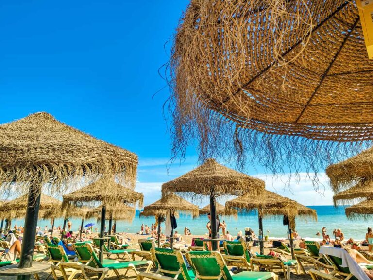 Rieten parasols en ligbedden op het zonnige Malagueta-strand in Málaga, met de Middellandse Zee op de achtergrond.