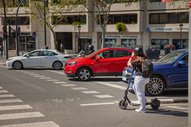 Gebruiker van een elektrische step met helm wacht bij een kruispunt tussen auto's in de Spaanse stad Valencia.