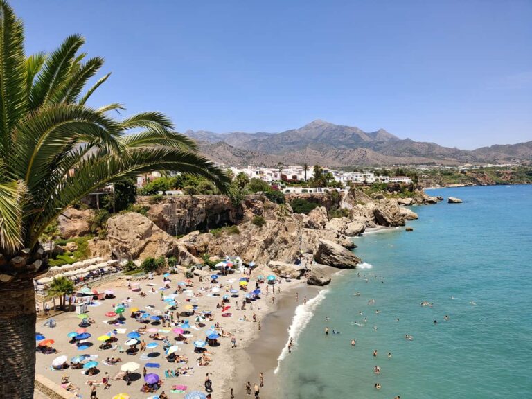 Zomers strand van Burriana in Nerja met badgasten, helderblauwe zee en bergen op de achtergrond in juni 2026.
